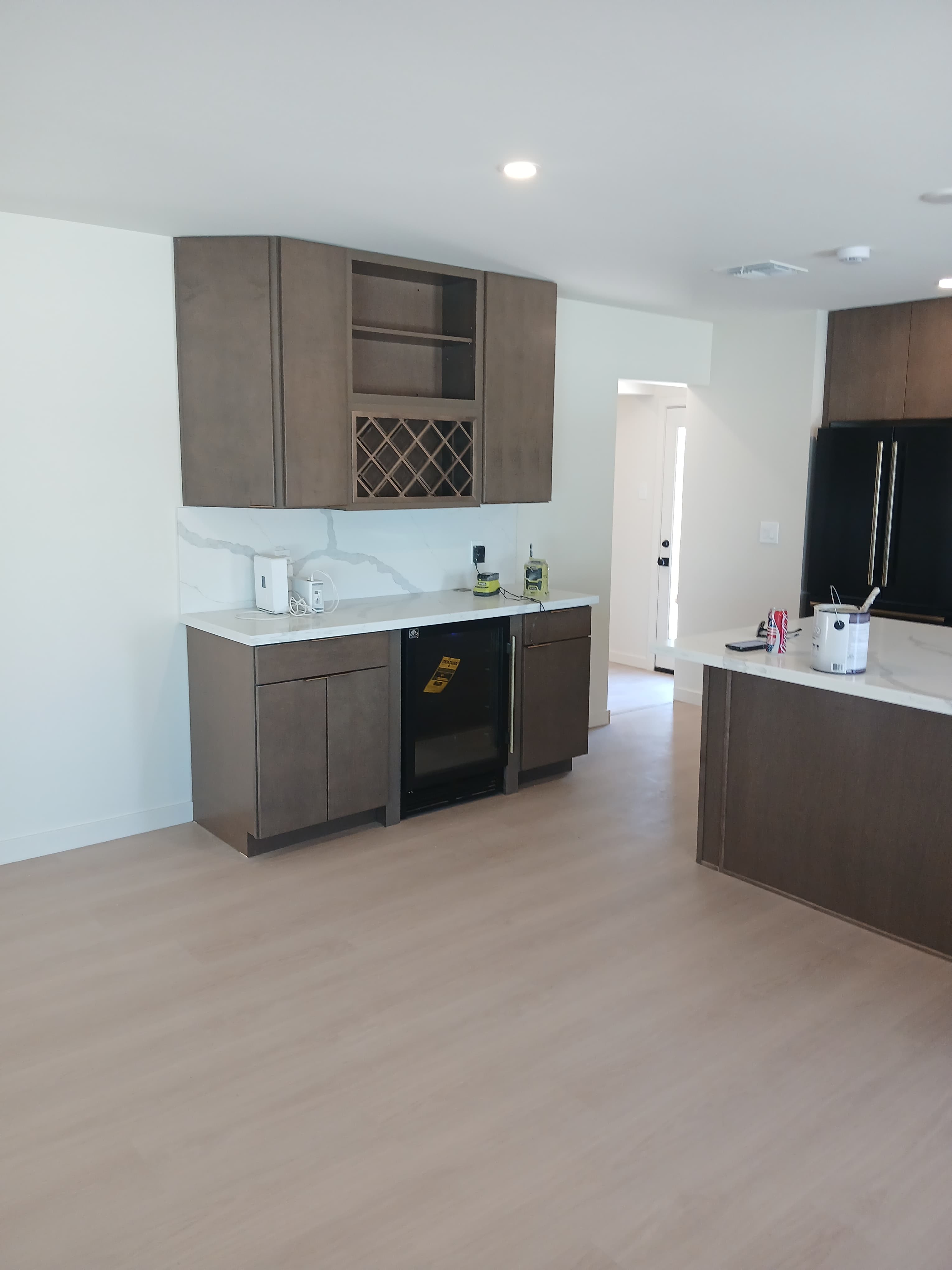 Modern bar featuring brown cabinets, a wine rack, beverage fridge, and white marble countertops.