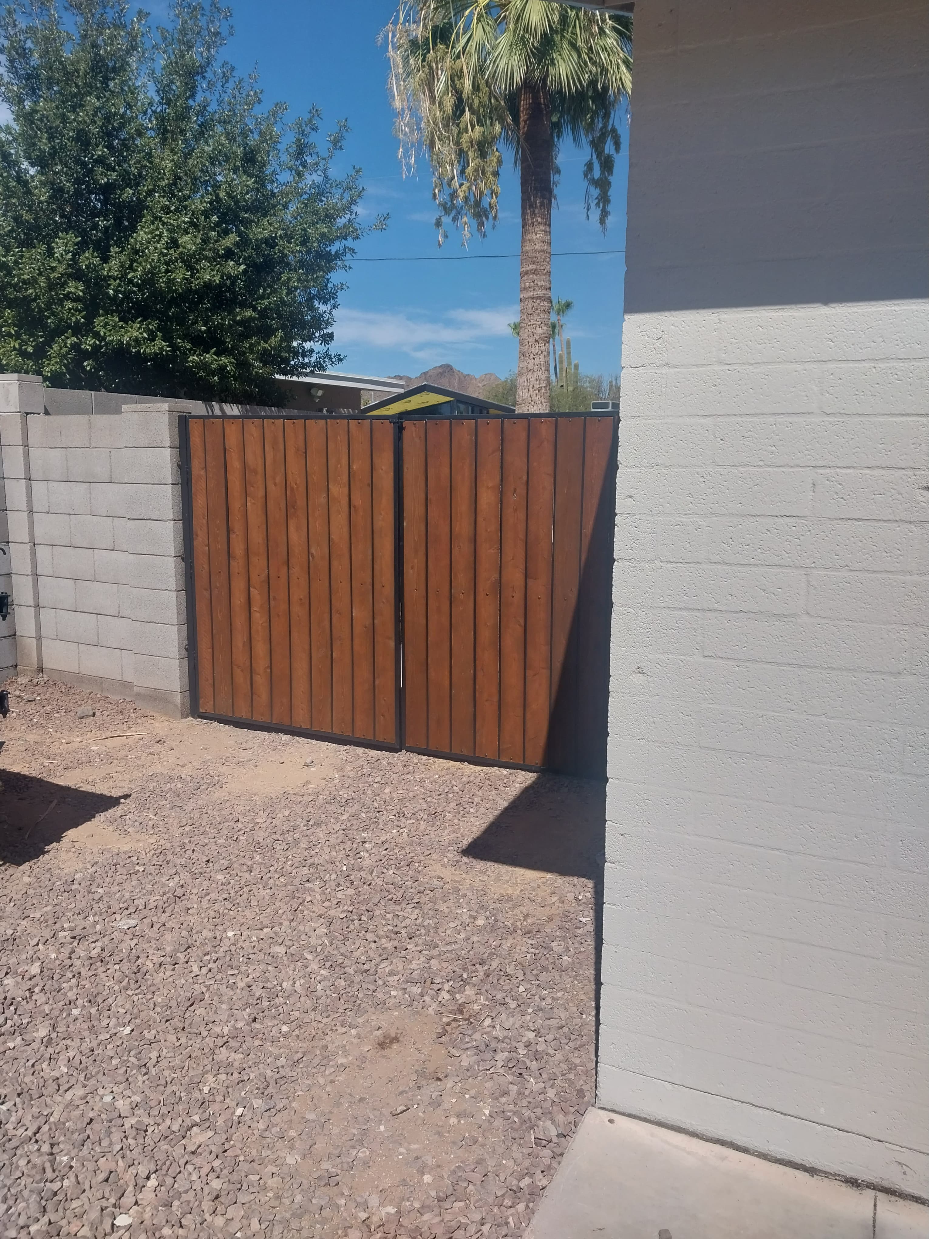 Stained wooden double gate with black frame between a block wall and white building.